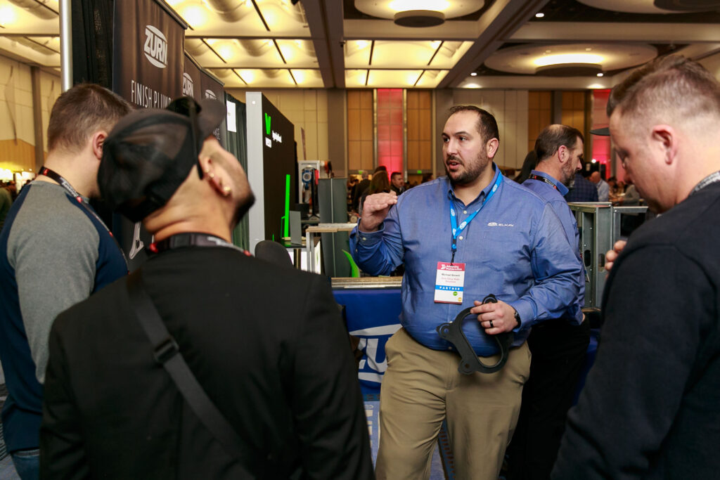 A picture of audience members speaking with a sponsor at last year's Advancing Prefabrication summit